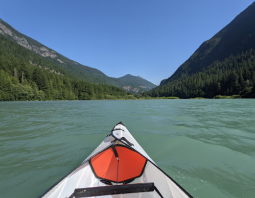 A kayak on a calm, green river surrounded by lush mountains under a clear blue sky.