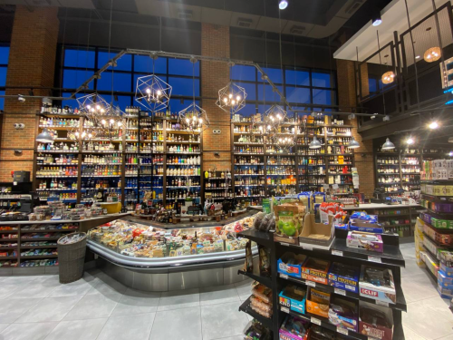 A modern store interior with shelves filled with various products, a display case of snacks, and stylish lighting.
