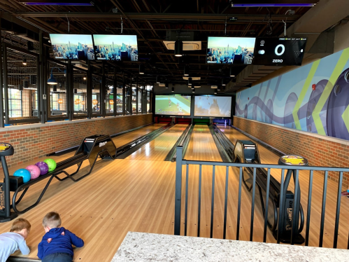 A bowling alley with colorful balls, empty lanes, and screens displaying scores in a modern setting.
