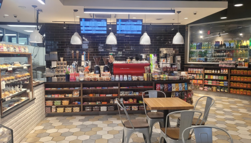 A modern café interior with a counter displaying snacks, drinks, and pastries, plus seating areas and digital menus.