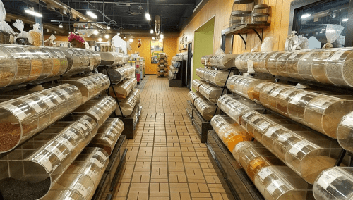 A spacious aisle in a store lined with clear containers of various spices and grains on shelves.