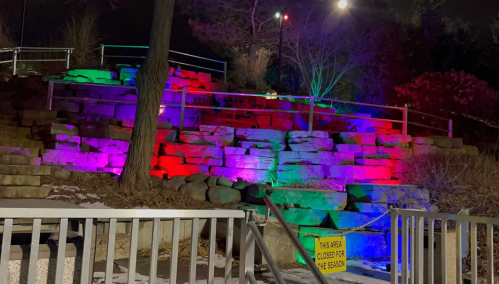 Colorful lights illuminate a stone wall and steps at night, with a sign indicating the area is closed for the season.