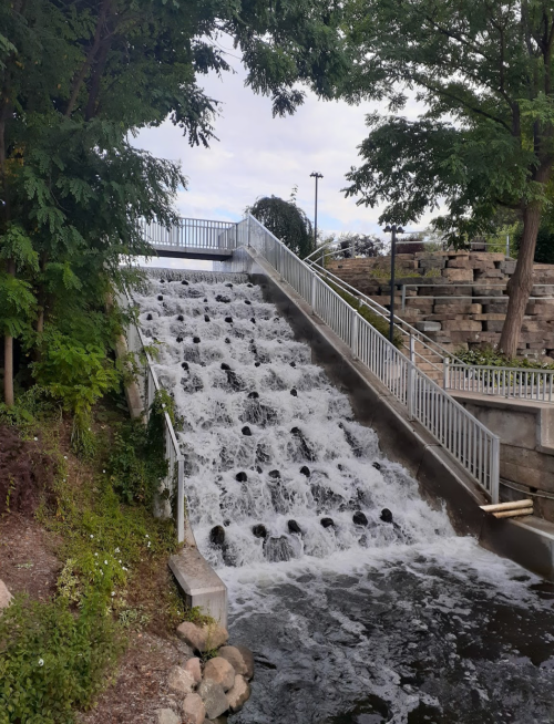 A cascading waterfall flows down a stepped structure, surrounded by greenery and stone landscaping.