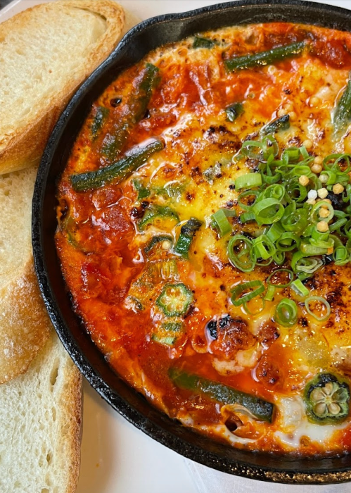 A skillet dish with baked eggs, green beans, and tomatoes, served with two slices of toasted bread on the side.