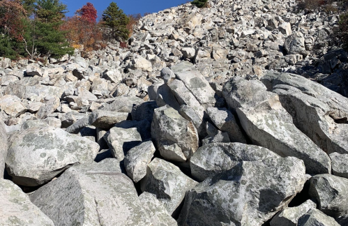 A rocky landscape filled with large boulders and scattered stones under a clear blue sky.