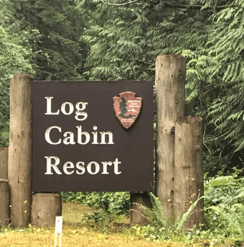 Sign for Log Cabin Resort surrounded by lush greenery and wooden posts.