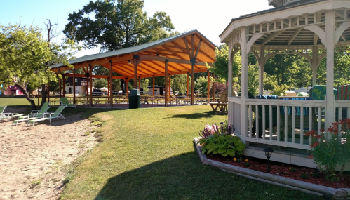 A sunny outdoor area featuring a gazebo, picnic pavilion, and sandy beach with lounge chairs.