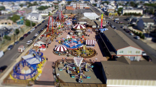 Aerial view of a vibrant amusement park with rides, games, and colorful tents, bustling with visitors.