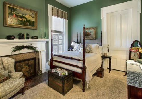 Cozy bedroom with green walls, a four-poster bed, vintage decor, and a fireplace, creating a warm, inviting atmosphere.