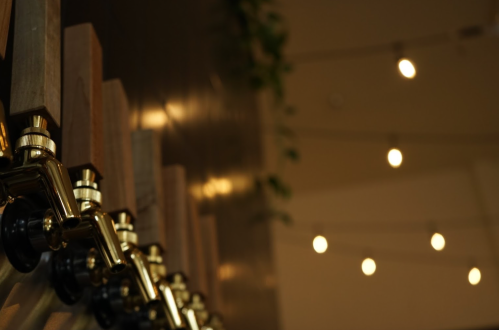A close-up of beer taps with a blurred background of warm, hanging lights.