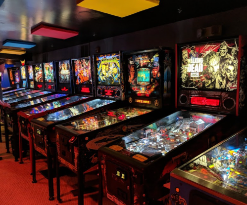 A row of colorful pinball machines in a dimly lit arcade, featuring various themes and designs.