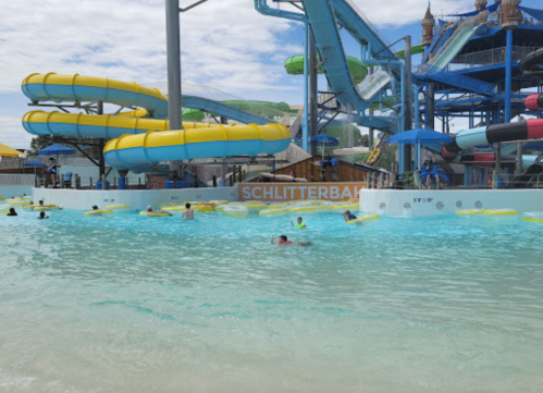 A water park scene with yellow slides, a wave pool, and people floating on tubes under a cloudy sky.