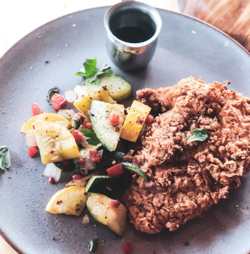 A plate with crispy fried chicken, a side of mixed sautéed vegetables, and a small cup of sauce.