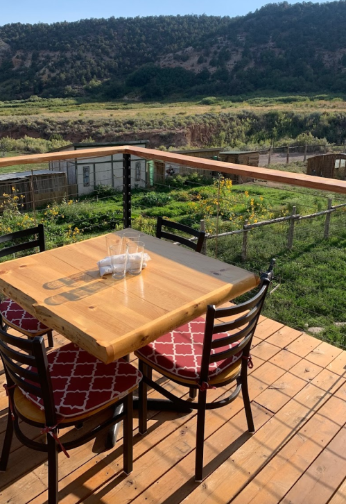 A wooden table with chairs on a deck overlooking a green field and hills in the background.
