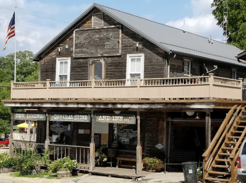 A rustic general store and inn with a wooden facade, porch, and American flag, set in a quaint outdoor setting.