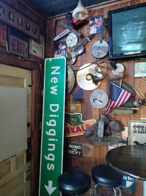A cozy bar corner featuring a green "New Diggings" sign, vintage decor, and a TV on the wall.