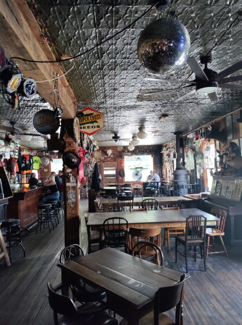 A rustic bar interior with wooden tables, a disco ball, and vintage decor on the walls.