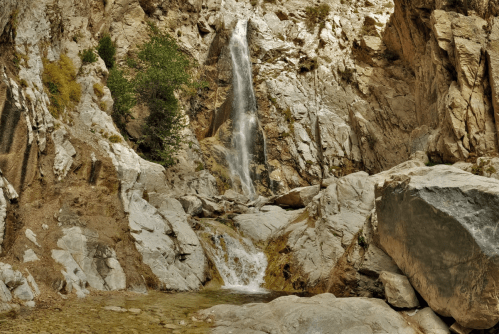 A serene waterfall cascading down rocky cliffs, surrounded by rugged terrain and sparse greenery.