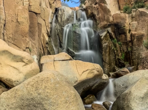 A serene waterfall cascading over rocky cliffs, surrounded by large boulders and greenery.