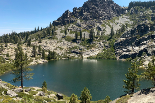 A serene mountain lake surrounded by rocky terrain and pine trees under a clear blue sky.