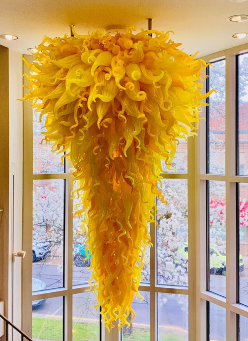 A vibrant yellow chandelier with swirling, organic shapes hangs from the ceiling, illuminated by natural light.