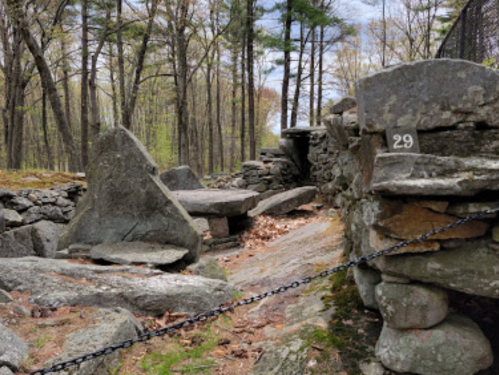 Stone structures and a pathway surrounded by trees, with a numbered stone marker in a forested area.