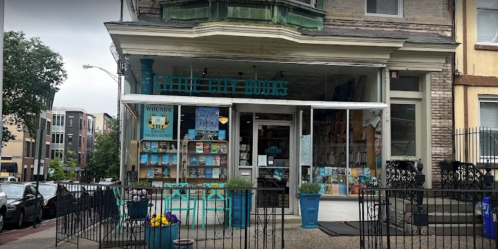 A charming bookstore with blue accents and potted plants, featuring large windows and a welcoming entrance.