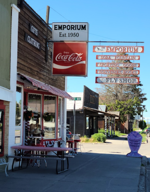 A quaint emporium storefront with a Coca-Cola sign, featuring gifts, clothing, and a toy shop in a small town.