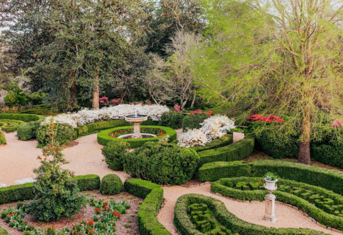 A beautifully landscaped garden featuring manicured hedges, colorful flowers, and a central fountain.