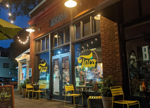Exterior of Bull Taco restaurant at night, featuring bright signage and outdoor seating under string lights.