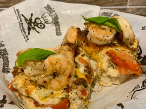 Two shrimp-topped biscuits with cheese and herbs, served on parchment paper.