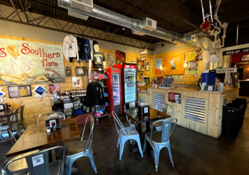 Interior of a casual restaurant with wooden walls, metal chairs, pirate-themed decor, and a drink cooler.