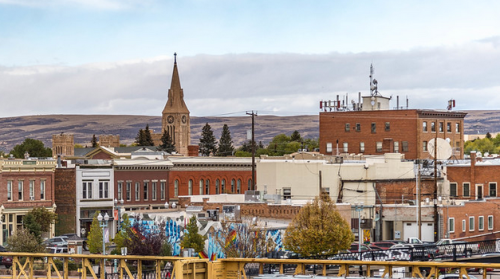 A scenic view of a small town with historic buildings, a church steeple, and mountains in the background.