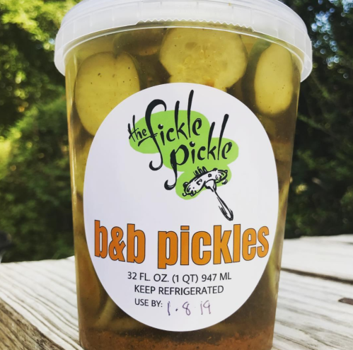 A clear container of b&b pickles with a colorful label, indicating it's from "The Fickle Pickle."