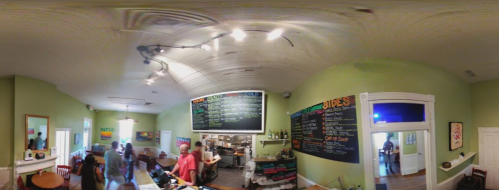 A cozy café interior with a chalkboard menu, patrons, and a bright green wall. Warm lighting enhances the inviting atmosphere.