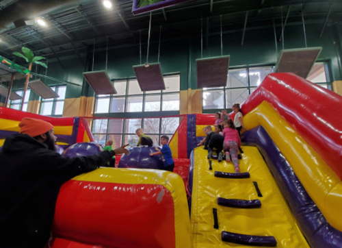 Children climbing and playing on colorful inflatable structures in a bright indoor space.