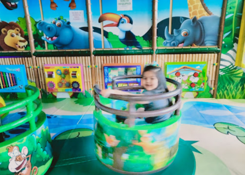 A child spins joyfully in a colorful play area with animal-themed decorations and vibrant surroundings.
