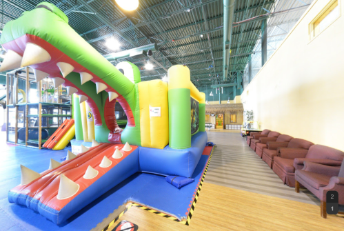 A colorful inflatable crocodile slide in a play area, with seating in the background and bright, spacious surroundings.