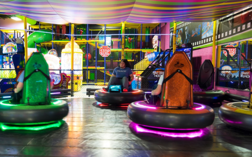 A colorful indoor amusement area with bumper cars and vibrant play structures in the background.