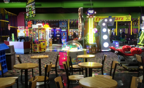 Brightly lit arcade with colorful games, empty tables, and vibrant decor, creating a fun, playful atmosphere.