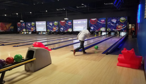 A person bowls in a modern bowling alley with colorful balls and screens in the background.
