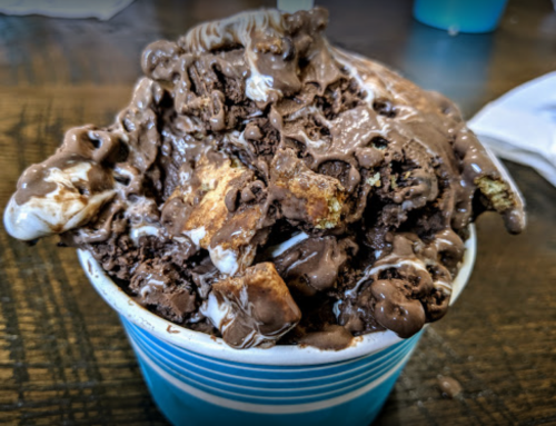 A cup overflowing with chocolate ice cream, mixed with chunks of cookie and drizzled with chocolate sauce.