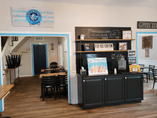 Interior of an ice cream shop with a service counter, seating area, and a welcoming sign.