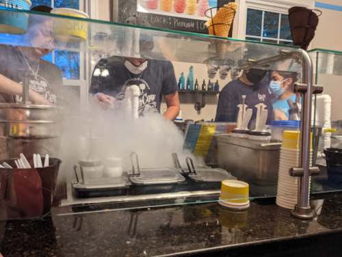 A dessert shop counter with staff preparing ice cream, surrounded by fog from liquid nitrogen.