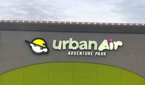 Exterior of Urban Air Adventure Park, featuring a bright sign and a person walking by the entrance.