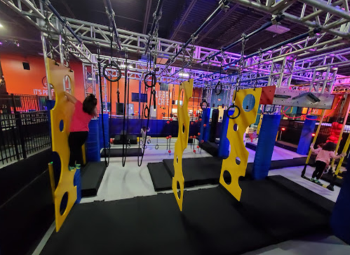 A colorful indoor playground with climbing structures and hanging rings, featuring children playing and exploring.