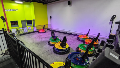 A colorful bumper car arena with several bumper cars arranged on a concrete floor, surrounded by a black railing.