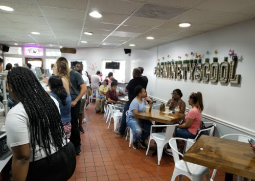 A busy café interior with people socializing, sitting at tables, and a sign that reads "SWEET & COOL" on the wall.