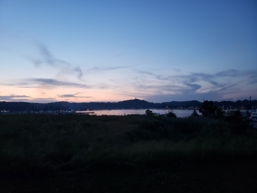 A serene twilight scene over a calm lake, with boats docked and distant hills under a colorful sky.