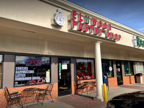 Exterior of Elmwood Pastry Shop with a sign, outdoor seating, and a window displaying "OPEN" and menu items.